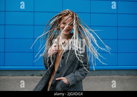 Secouant les bandes de roulement légère adolescente devant un panneau bleu de la couverture murale. Elle porte une veste à carreaux grise. Portrait. Banque D'Images