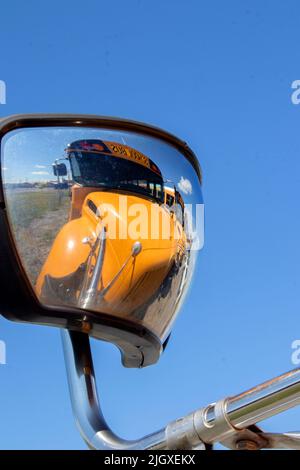 Un grand autobus scolaire jaune se reflète dans le miroir latéral du bus en face de lui apportant un sentiment moderne et abstrait au transport d'éducation publique Banque D'Images