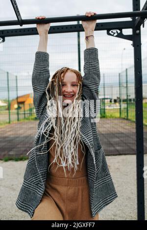 Freckled adolescente avec des bandes accrochées sur un bar haut sur le terrain de sport. Regarder la caméra. Banque D'Images