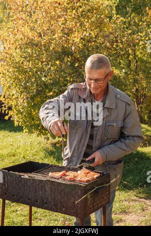 Homme senior qui fait griller de la viande le jour de l'automne Banque D'Images