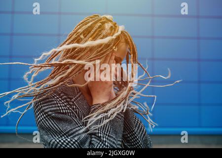 Une adolescente légère secoue devant un panneau de recouvrement bleu. Elle porte une veste à carreaux grise. Portrait. Banque D'Images