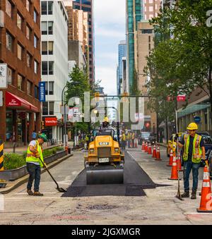 Une équipe de travailleurs a mis l'asphalte chaud sur une route. Travailleurs de la construction routière avec des pelles en uniformes de protection. Travaux de construction routière dans une ville-1 juillet Banque D'Images