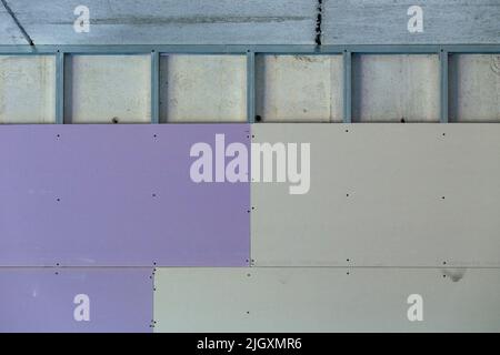cloison sèche mauve et grise installée sur des montants en acier galvanisé reliés sur un mur en béton d'un bâtiment commercial Banque D'Images