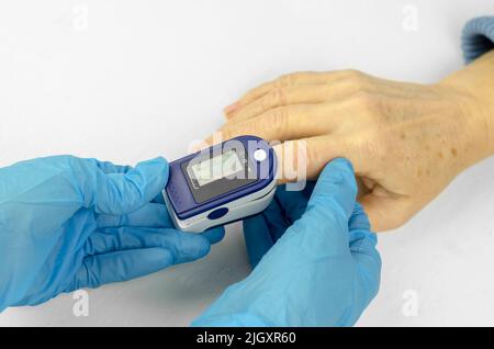 Mains du médecin en gants médicaux appliquez un oxymètre de pouls sur le doigt d'une femme âgée. Mesurer la satiété chez une femme asiatique de 60 ans. Entretien Banque D'Images