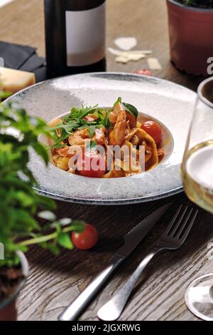 Gros plan sur des pâtes de fruits de mer avec sauce et tomates cerises servies avec du vin blanc. Plat principal, concept de plat de restaurant Banque D'Images