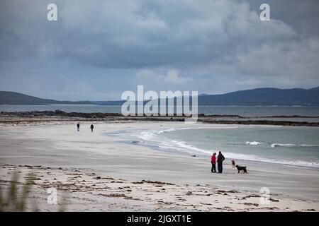 Une femme au pelage rouge, avec d'autres personnes et des chiens sur la plage de Gearraidh na Monadh sur l'Uist du Sud dans les Hébrides. Banque D'Images