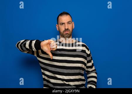 Espagnol homme avec la barbe déplaisait posant isolé sur le mur bleu arrière-plan studio portrait. Les gens ont candide émotions concept de style de vie. Copie de maquette Banque D'Images