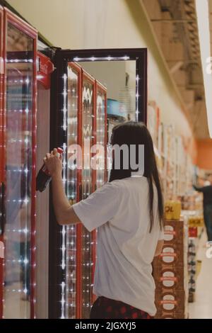 une jeune fille attrapant une bouteille de soda sur le réfrigérateur Banque D'Images