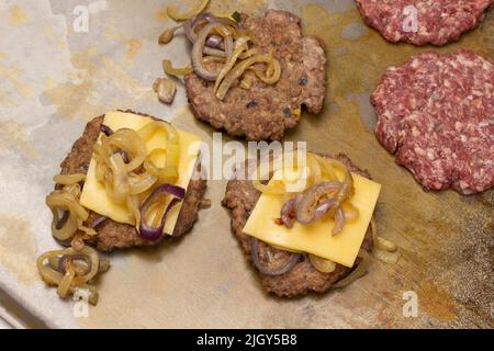 Hamburgers frits avec fromage et oignons. Hamburgers crus sur fond métallique rouillé. Vue de dessus Banque D'Images