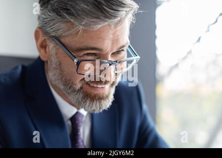 Gros plan sur un homme d'affaires heureux d'âge moyen portant des lunettes assis au bureau Banque D'Images