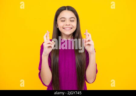 Un adolescent tenant les doigts croisés pour Bonne chance. La jeune fille prie et espère que les rêves deviennent vrais, isolé sur fond jaune. Banque D'Images