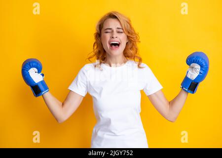 Gagnante boxer féminin avec ses mains soulevées excitée. Isolé sur fond jaune. Femme excitée en gants de boxe. Criant boxeur jeune femme forte. Banque D'Images