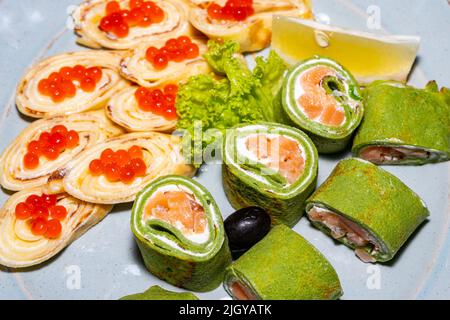 Quelques sushis verts avec du poisson rouge et des crêpes avec du caviar rouge gros plan. Banque D'Images