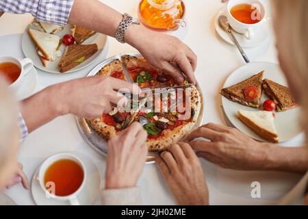 Directement au-dessus de la vue de l'homme méconnaissable avec montre-bracelet assis à table plein de collations et coupant de petites pizzas pour des amis Banque D'Images