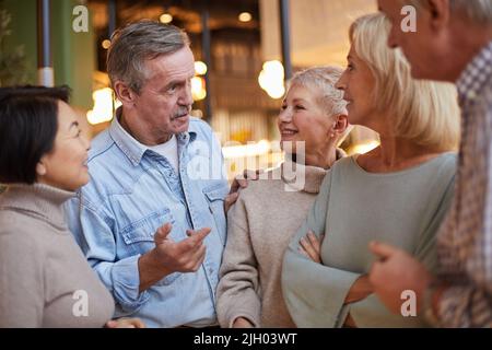 Homme âgé et confiant dans une chemise en Jean touchant l'épaule d'une amie féminine tout en partageant une histoire intéressante avec des amis Banque D'Images