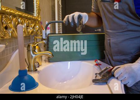 Image des mains d'un plombier en gants de travail tenant une serrure de cheveux qui bloquait l'évier. Faites-le vous-même les travaux ménagers Banque D'Images