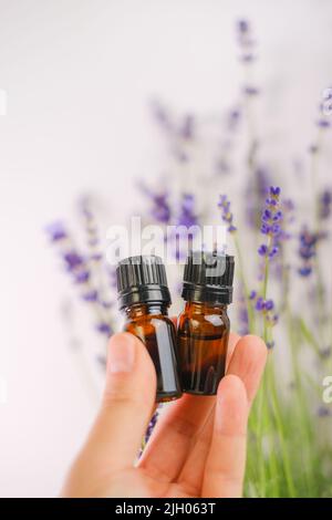 Huile essentielle de lavande dans des bouteilles de verre brun dans une main et fleurs de lavande sur un fond blanc.essence avec parfum de lavande. Aromathérapie et Banque D'Images