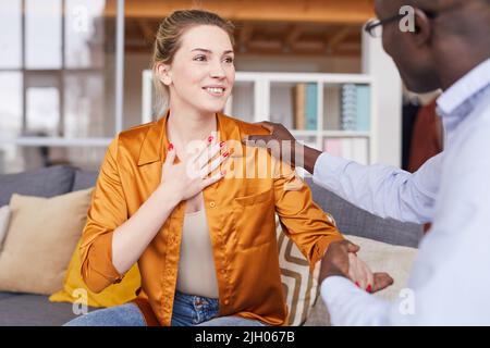 Bonne jeune femme attrayante en blouse de soie assise sur le canapé et remerciant thérapeute qui l'appuie à la session de psychologie Banque D'Images