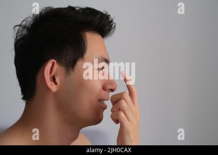 Profil visage de beau jeune homme asiatique appliquant des lentilles de contact Banque D'Images