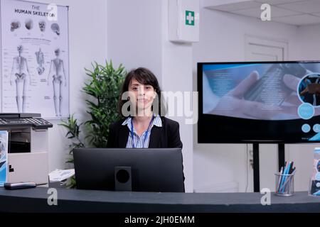 Portrait d'un réceptionniste souriant à la réception attendant d'accueillir les patients dans le hall de la clinique privée. Professionnel de la santé offrant un soutien pour les rendez-vous à l'hôpital. Banque D'Images