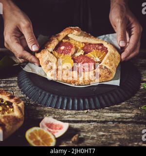 Mains de la récolte anonyme cuisinier tenant savoureux doux maison fraîchement cuit tarte avec des agrumes à la table en bois dans la cuisine légère Banque D'Images