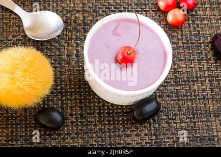 Mousse Jamun ou mousse Black Plum recouverte de cerises. Dessert vegan maison frais. Vue sur le dessus, gros plan du bol isolé sur fond sombre. Espace copie. Banque D'Images