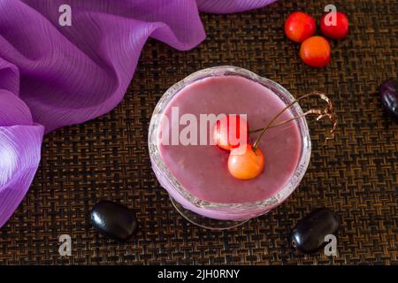 Mousse Jamun ou mousse Black Plum recouverte de cerises. Dessert vegan maison frais. Vue sur le dessus, gros plan du bol isolé sur fond sombre. Espace copie. Banque D'Images