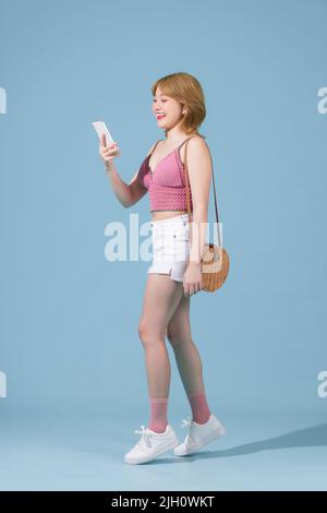 Jeune femme heureuse utilisant le téléphone portable marchant en allant isolé sur fond bleu pastel portrait de studio Banque D'Images