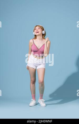 Insouciante femme asiatique belle-look proche des yeux et danse détendue avec le smartphone, écouter de la musique dans les écouteurs, chanter karaoké Banque D'Images