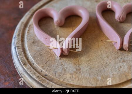 Les saucisses coupées dans le sens de la longueur sont disposées sur une planche à découper. Les saucisses sont disposées en forme de coeur. Cuisson du repas. Amour, conce de relation Banque D'Images