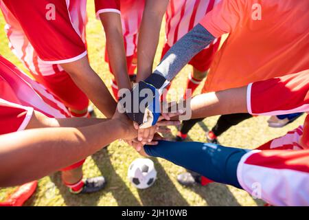 Vue en grand angle des joueurs de l'équipe de football multiracial masculins qui se empilent les mains avant le match sur le terrain de jeu Banque D'Images