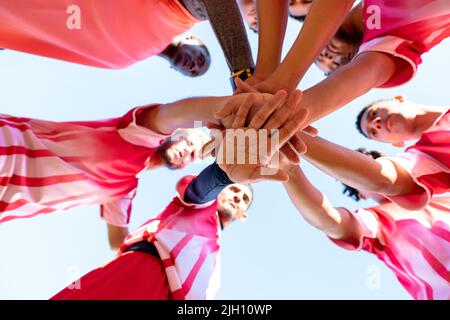 Vue en contre-plongée des joueurs de l'équipe de football multiracial masculins qui ont les mains empilées avant le match sur le terrain de jeu Banque D'Images