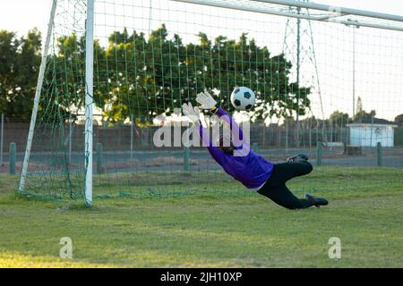 Gardien de but afro-américain aux bras levés pour attraper le ballon de football en plein air pendant le match Banque D'Images