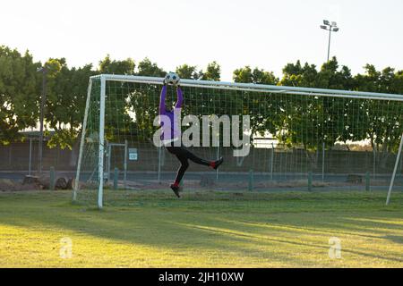 Gardien de but afro-américain aux bras levés sautant et attrapant le ballon de football en plein air Banque D'Images