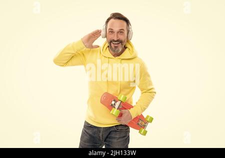 un homme souriant et expérimenté écoute de la musique isolée sur blanc. un homme en pull à capuche jaune avec planche à roulettes. Banque D'Images