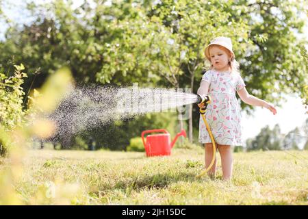 Adorable petite fille jouant avec un tuyau de jardin le jour d'été chaud et ensoleillé Banque D'Images