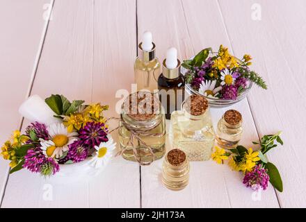 un ensemble d'huiles cosmétiques, organiques et essentielles dans différentes bouteilles sur une table en bois blanc avec plantes médicinales de prairie. attention sélective Banque D'Images