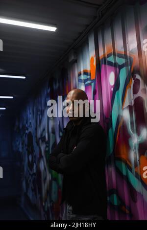 Un hooligan afro-américain croisant les bras près des graffitis sur le mur dans le garage Banque D'Images