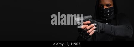 Un bandit afro-américain flou tenant une arme de poing isolée sur une bannière noire Banque D'Images