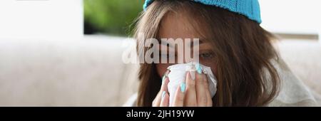 Une femme essuie le nez mouillé avec un mouchoir habillé d'un chapeau chaud et recouvert d'une couverture Banque D'Images