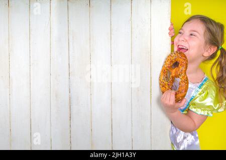 Concept de vacances allemand bavarois Oktoberfest. Drôle sourire mignon petit blond caucasien petite fille enfant dans la robe traditionnelle avec bretzel pâtisseries, on Banque D'Images