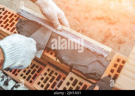 Le travailleur ou la couche de brique travaille avec des briques de pose de truelle. Le constructeur fait du brickwork sur le chantier de construction, en gros plan sur les mains. Banque D'Images