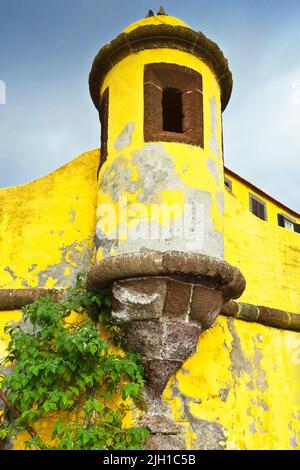 Une tour de défense avec des ébratures du fort Fortaleza de Sao Tiago à Funchal, sur l'île de Madère, peint en jaune vif contre un ciel bleu foncé. Banque D'Images