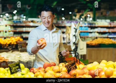 un jeune homme asiatique choisit et cueille dans un sac écologique des fruits ou des légumes de pomme dans le supermarché. un client de sexe masculin dans une épicerie près du comptoir achète et jette dans un emballage réutilisable sur le marché Banque D'Images