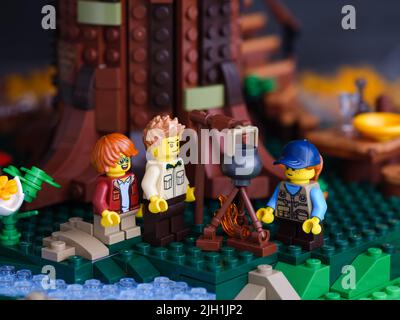 Tambov, Fédération de Russie - 22 juin 2022 trois mini-figurines Lego - père et deux enfants, debout sous un arbre et cuisinant de la nourriture sur un feu de camp. Banque D'Images