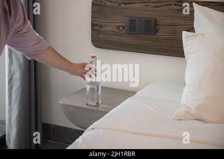 Gros plan des mains mettant la bouteille d'eau de boisson sur l'armoire devant le lit Banque D'Images