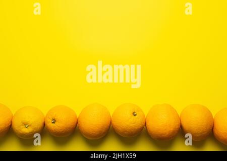 Poser à plat avec des oranges en ligne sur fond jaune Banque D'Images