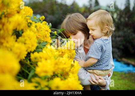 Une jeune fille et son frère admirent les fleurs jaune vif de rudbeckia, communément connues sous le nom de fleurs conées ou de susans à yeux noirs, dans un jardin d'été ensoleillé. Banque D'Images