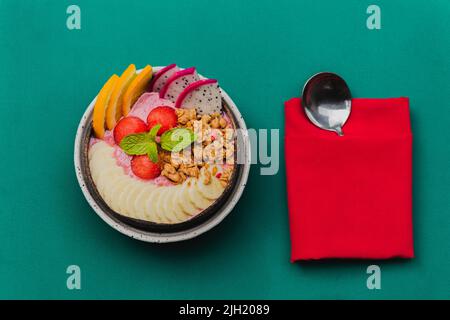 Bols à smoothie avec granola, et fruits mélangés sur fond vert. Banque D'Images