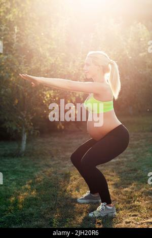Femme enceinte s'accroupidant à l'extérieur, lumière du lever du soleil Banque D'Images